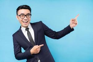 asiatischer Geschäftsmann im Anzug, der auf blauem Hintergrund zeigt