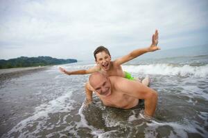 glücklich Junge schwimmt und Theaterstücke mit Opa oder Papa auf das Strand. foto