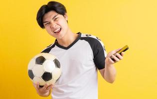 asiatischer Mann hält einen Ball und hält ein Telefon in der Hand