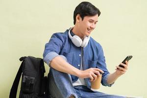 Hübscher asiatischer Studentenjunge, der mit Smartphone sitzt foto