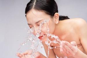 schöne asiatische frau wäscht ihr gesicht mit reinem wasser foto