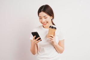 Porträt des jungen asiatischen Mädchens, das Kaffeetasse hält und Telefon benutzt foto