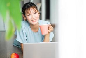 junge asiatische frau, die ein dokument liest und einen laptop benutzt, wenn sie von zu hause aus arbeitet