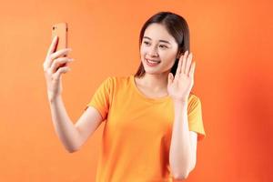Bild der jungen Asiatin mit Smartphone auf orangem Hintergrund foto
