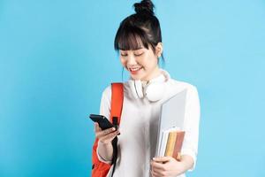 Asiatische Studentin, die Rucksack hinter dem Rücken trägt, Smartphone hält, Hals mit drahtlosen Kopfhörern, Pappbecher hält holding foto