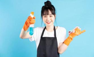asiatische Hausfrau trägt orangefarbene Handschuhe und hält einen Wasserstrahl in der Hand