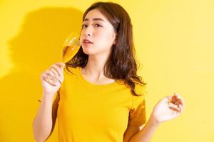 junge asiatische frau trinkt wein und posiert auf gelbem hintergrund