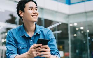Bild eines jungen asiatischen Mannes, der Smartphone lächelt und benutzt