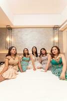 ein Gruppe von asiatisch Frauen im schön Kleider Sitzung zusammen auf ein Weiß Bett während bleiben foto