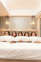 ein Gruppe von asiatisch Frauen sind Schlafen und gelehnt auf Weiß Kissen mit ihr freunde im ein Luxus Hotel foto