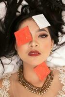 ein asiatisch Frau mit ein Gold Halskette Stürze schlafend mit ein Kondom Verpackung auf ihr Gesicht im ein Hotel foto