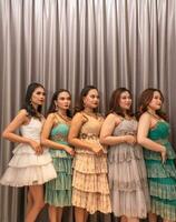 ein Gruppe von asiatisch Frauen sind Stehen im Vorderseite von das Vorhänge von ein Luxus Hotel während tragen Kleider beim ein Party foto