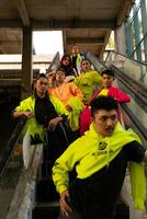 ein Gruppe von asiatisch Männer im Zitrone Grün Jacken sind Stehen mit ihr freunde auf das Rolltreppe foto