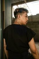 ein asiatisch Mann hängend von das Eisen von ein verlassen Gebäude während tragen ein schwarz Hemd foto