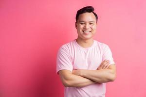 asiatischer Mann, der mit verschränkten Armen auf rosafarbenem Hintergrund steht