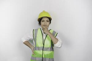 ein nachdenklich jung Frau Arbeit Arbeiter tragen Sicherheit Helm und Weste ist suchen beiseite zu ein Idee auf Kopieren Raum , isoliert durch Weiß Hintergrund. Arbeit Tag Konzept. foto