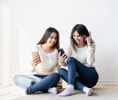 Zwei schöne Freundinnen senden Nachrichten mit Mobiltelefonen foto