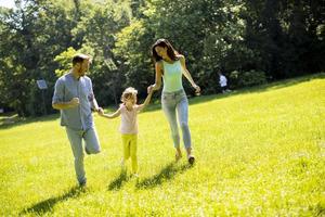glückliche junge Familie mit süßer kleiner Tochter, die an einem sonnigen Tag im Park läuft