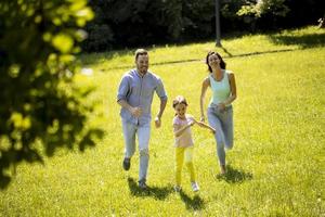 glückliche junge Familie mit süßer kleiner Tochter, die an einem sonnigen Tag im Park läuft foto