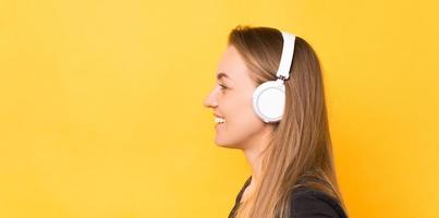 Seitenansichtporträt einer lächelnden Frau mit weißen drahtlosen Kopfhörern auf gelbem Hintergrund