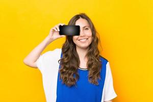 lächelnde junge Frau mit Smartphone mit leerem Bildschirm auf gelbem Hintergrund foto