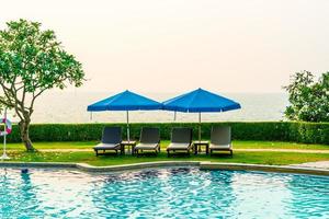 Liegestühle oder Poolbetten mit Sonnenschirmen um den Pool bei Sonnenuntergang