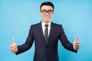 asiatischer Geschäftsmann, der Daumen auf blauem Hintergrund aufgibt