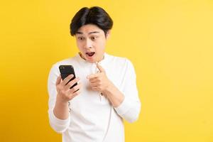 asiatischer Mann, der auf Telefon auf gelbem Hintergrund zeigt