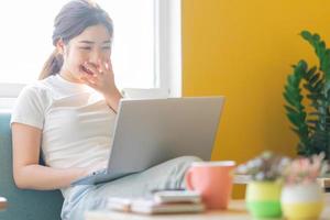 junge Asiatin sitzt auf dem Sofa und arbeitet zu Hause at foto