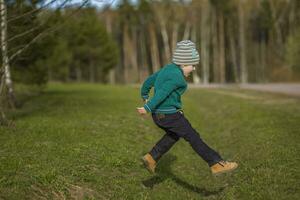 komisch Junge Spaziergänge im das Frühling Park, läuft, springt und genießt. foto