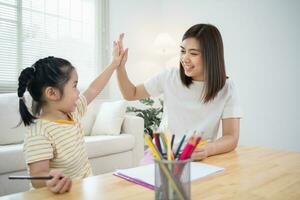 süß wenig Kind und Mama Hände Herstellung geben mich fünf während Gemälde mit bunt malt. asiatisch Mädchen und Mutter mit Wachsmalstift Zeichnung Farbe. Tochter und Mama tun Hausaufgaben Färbung Karikatur Figuren. foto