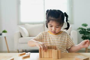 asiatisch Mädchen Kind Tochter lächelnd glücklich und Lachen spielen hölzern Spielzeug Turm Sitzung auf Sofa Couch im Leben Zimmer beim heim, Baby Kinder Aktivitäten spielen glücklich Spiele. Familie Aktivität Konzept. foto