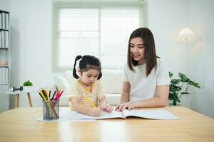 süßes kleines kind, das mit bunten farben malt. asiatische Mädchen und Mutter mit Zeichenstiftfarbe. tochter und mutter machen hausaufgaben zum färben von zeichentrickfiguren. baby-künstler-aktivität-lifestyle-konzept. foto