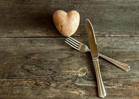 rote Kartoffeln in Herzform auf einem hölzernen Hintergrund mit Gabel und Messer. das Konzept der Landwirtschaft, Ernte, Vegetarismus. Valentinstag. quadratisches, hässliches Essen. foto