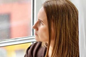Porträt einer jungen nachdenklichen Frau, die am Fenster sitzt. Nahansicht
