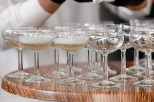 Sekt, Champagner in Gläsern auf dem Holztisch. Kellner in schwarzen Handschuhen gießt im Restaurant Alkohol in Gläser. selektiver Fokus