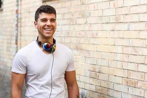 junger Mann im städtischen Hintergrund, der mit Kopfhörern Musik hört foto