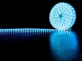 Spule aus LED-Streifen für dekorative Beleuchtung, Diodenstreifen mit blauem Kaltlicht auf dunklem Hintergrund foto