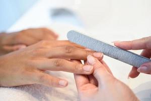 Frau in einem Nagelstudio, die eine Maniküre mit Nagelfeile erhält foto