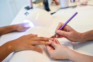Nahaufnahme der Kosmetikerin, die die Nägel einer Frau mit einem Pinsel in einem Nagelstudio malt foto