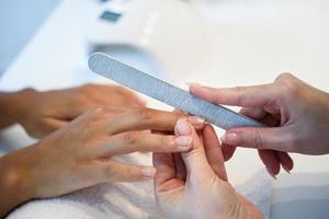 Frau in einem Nagelstudio, die eine Maniküre mit Nagelfeile erhält foto