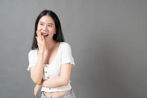 junge asiatische frau mit glücklichem und lächelndem gesicht im weißen hemd auf grauem hintergrund