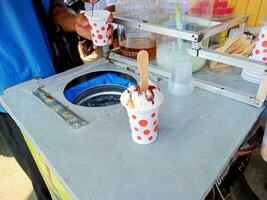 Straße Eis Sahne Anbieter sind Herstellung Aufträge zum Süss Eis Sahne gemischt mit Stücke von brot, Jackfrucht und gesüßt kondensiert Milch während das Tag foto