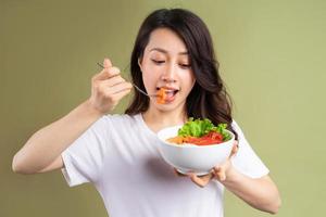 fröhliche junge asiatische Frau, die gesundes Essen im Hintergrund isst foto