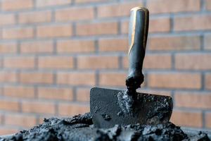 Maurerkelle in frischem Mörtel mit Ziegelwand im Hintergrund. foto