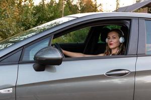 Am Steuer des Autos sitzt eine junge, schöne Frau mit langen Haaren und Kopfhörern. foto