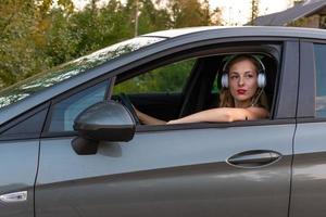 Am Steuer des Autos sitzt eine junge, schöne Frau mit langen Haaren und Kopfhörern. foto