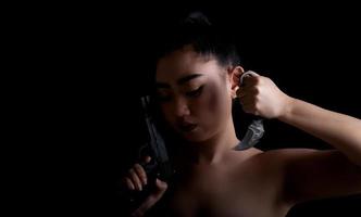 Asiatin mit einer Hand, die eine Waffe und ein Karambit-Messer am schwarzen Hintergrund hält foto