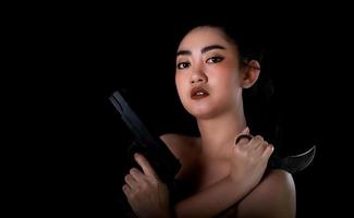 Asiatin mit einer Hand, die eine Waffe und ein Karambit-Messer am schwarzen Hintergrund hält foto
