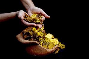 Münzgold in der Hand auf Losen, die goldene Münzen in zerbrochenem Schatzglas mit weißem Hintergrund stapeln foto